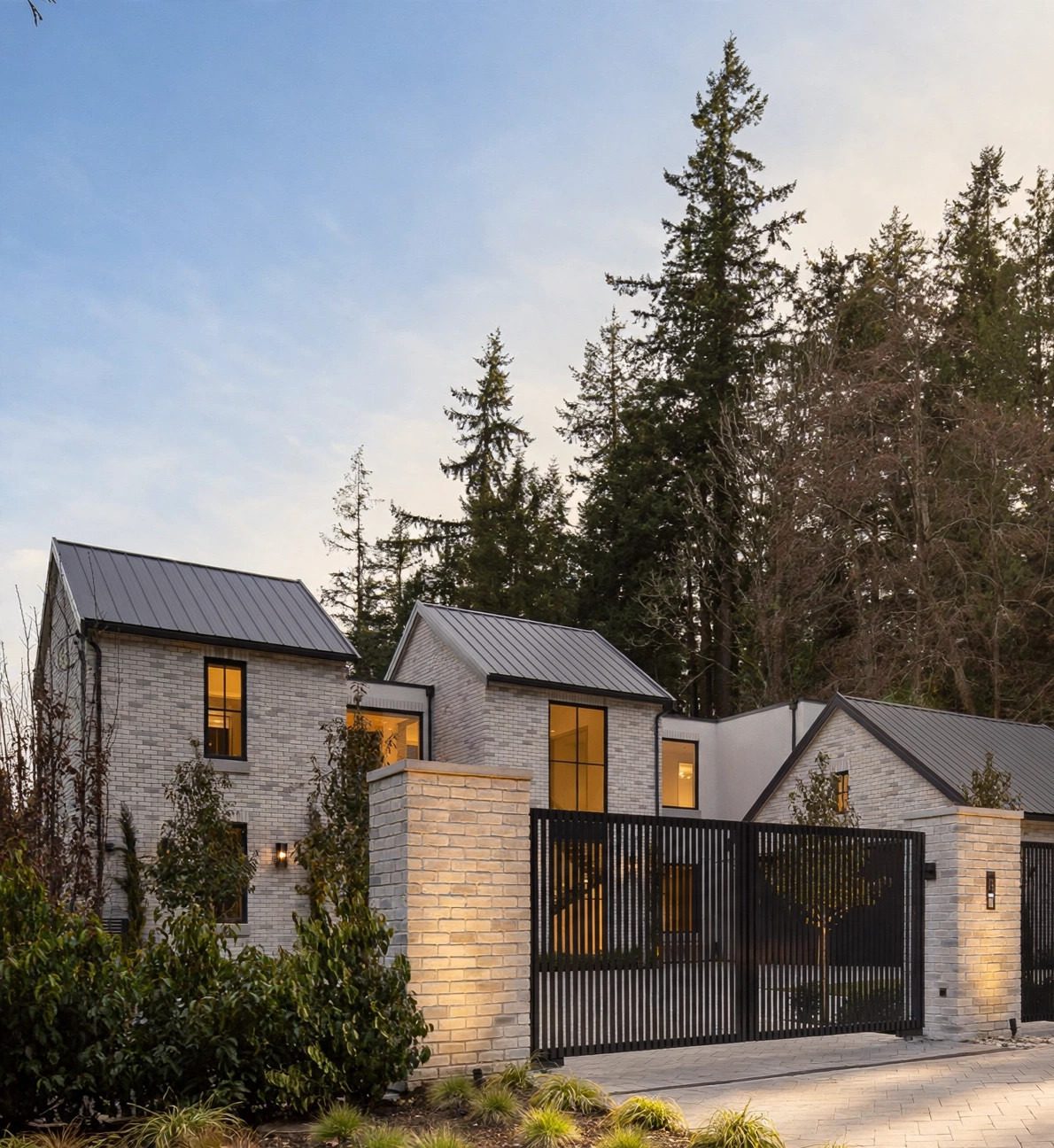 Gated white-brick residence set against mature evergreens at dusk