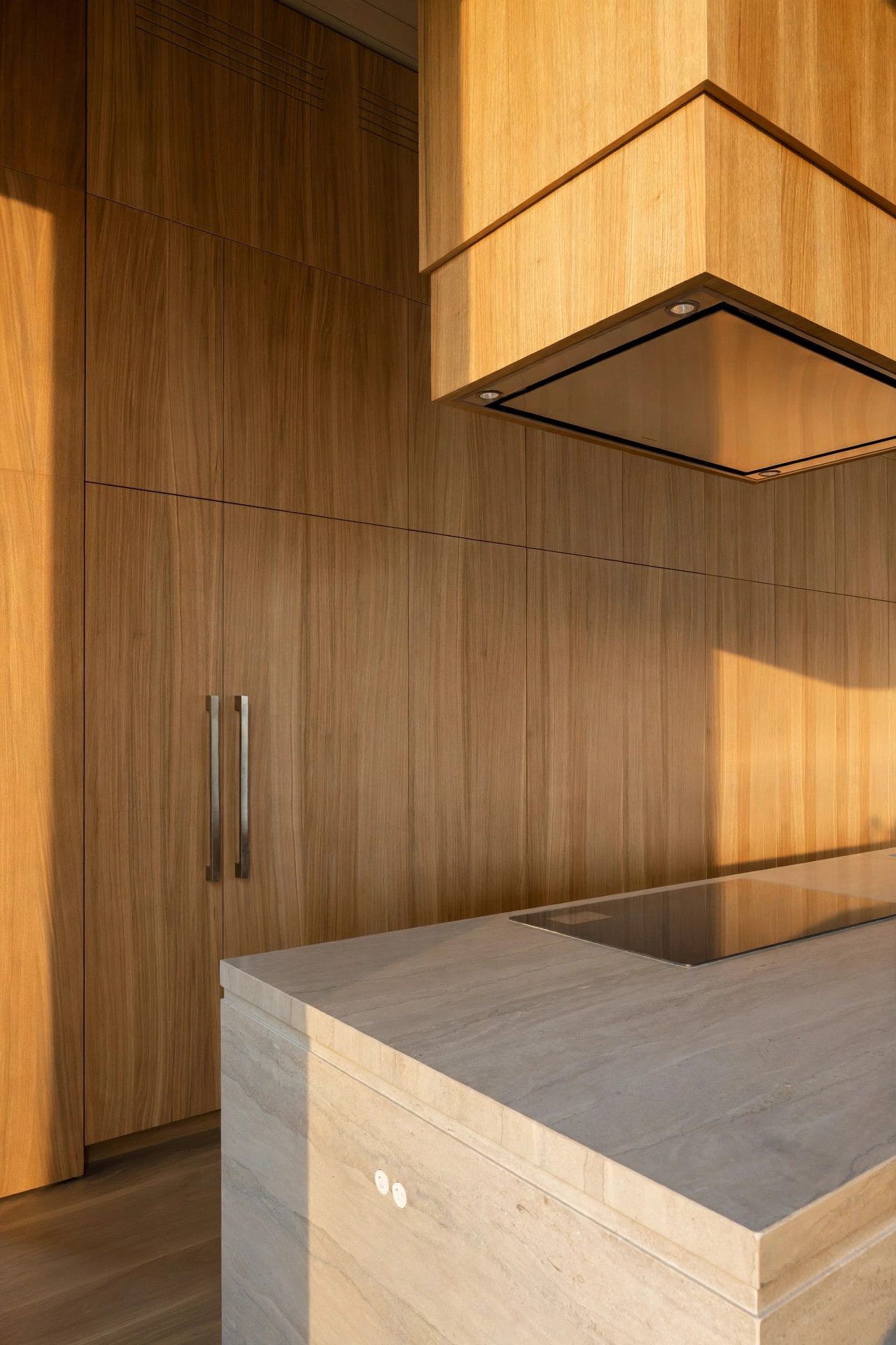 Warm oak kitchen millwork and stone island in late-day light