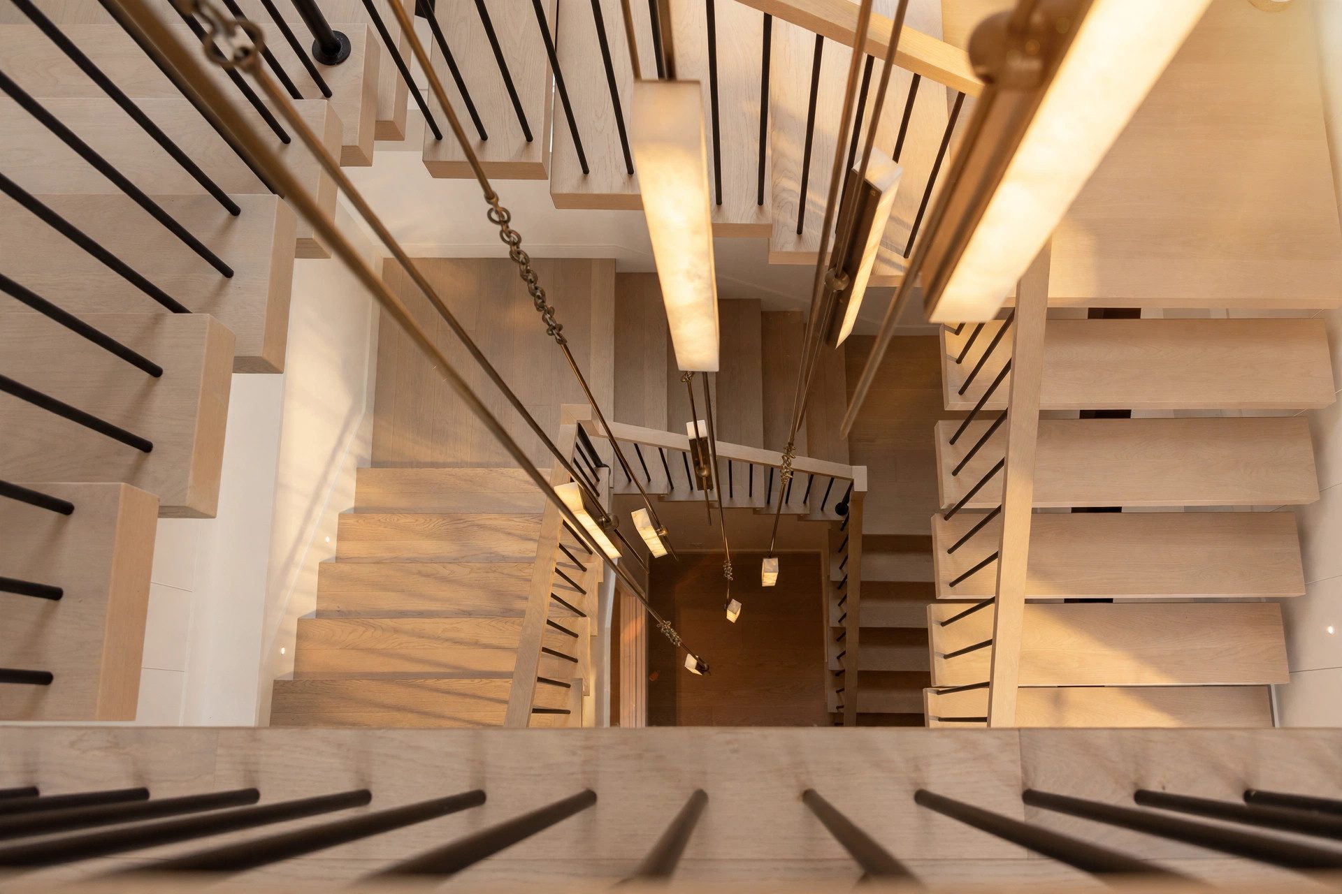 Top-down view through a light oak staircase with black metal railings